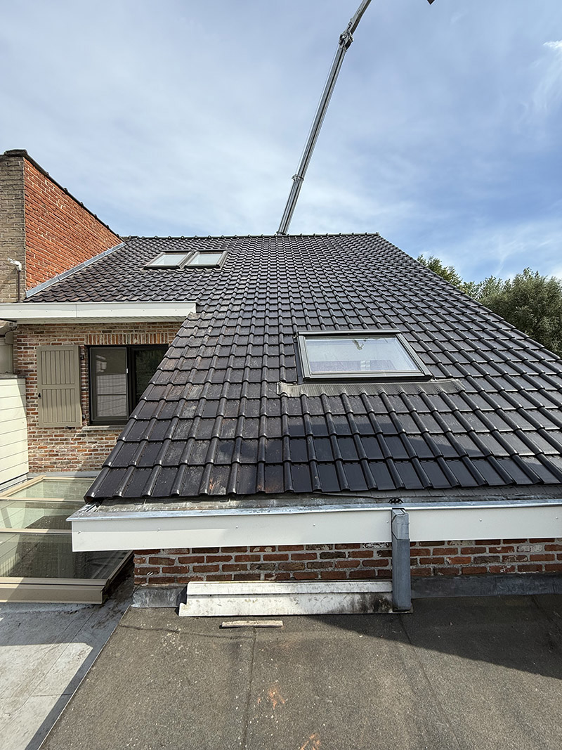 Na de dakrenovatie in Aalst, met nieuwe donkere keramische dakpannen en verzorgde afwerking.
