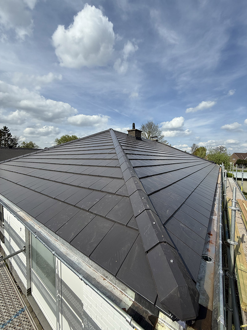Na de dakrenovatie in Ninove, afgewerkt met moderne donkere dakpannen.