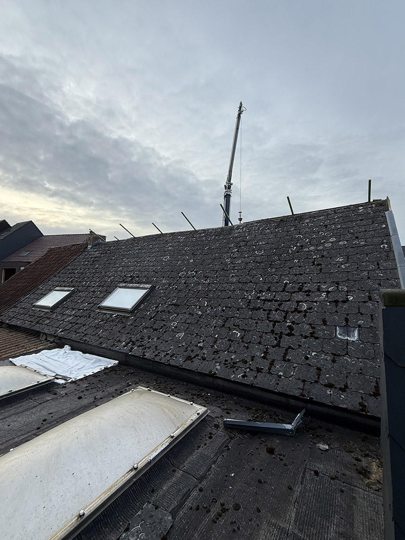 Voor de dakrenovatie in Oudenaarde, oude leien met mos en slijtage zichtbaar.